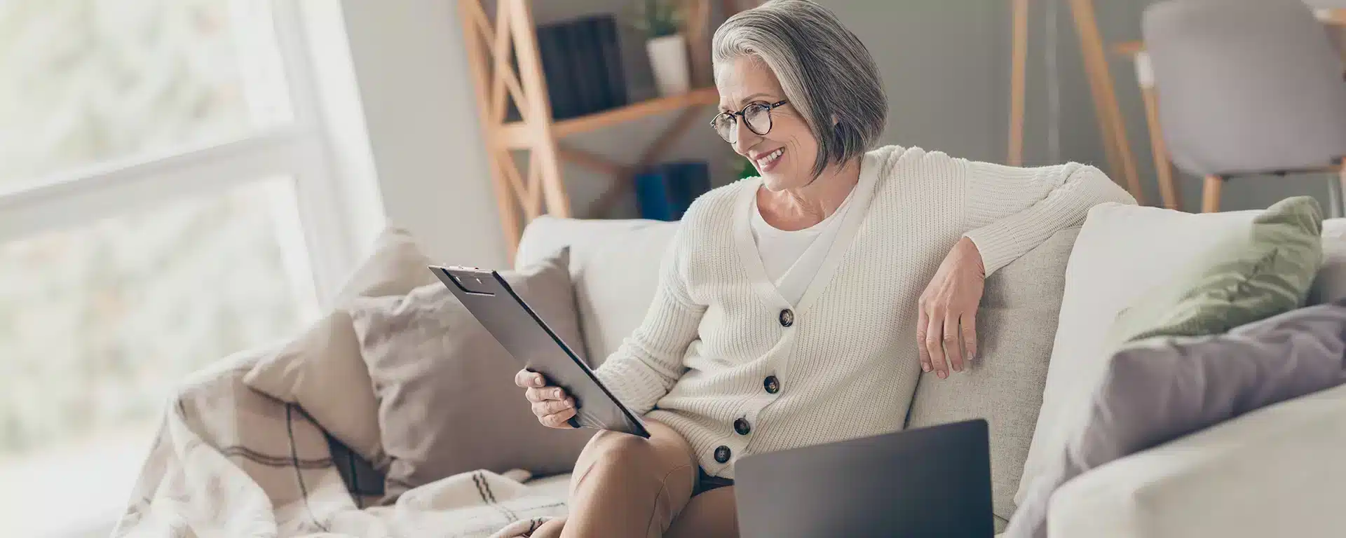 Senior woman reading a notepad while sitting on a comfortable looking sofa.